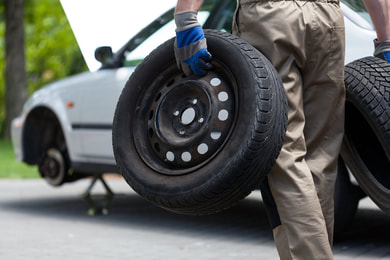 Man holding two black sedan tires, performing flat tire repair in St. George, UT